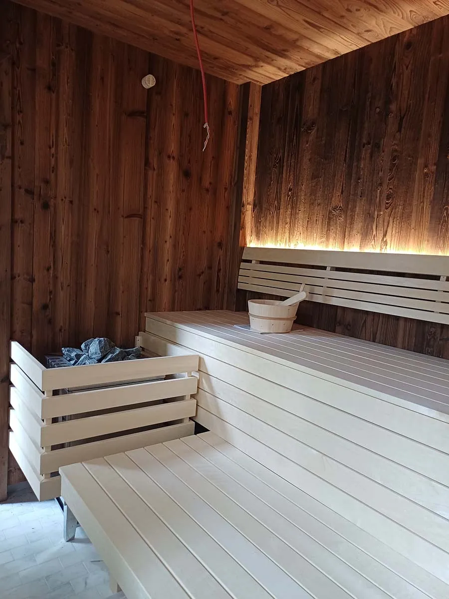 Bio-Sauna in dunklem Holz mit indirekter Beleuchtung und Aufgusskübel