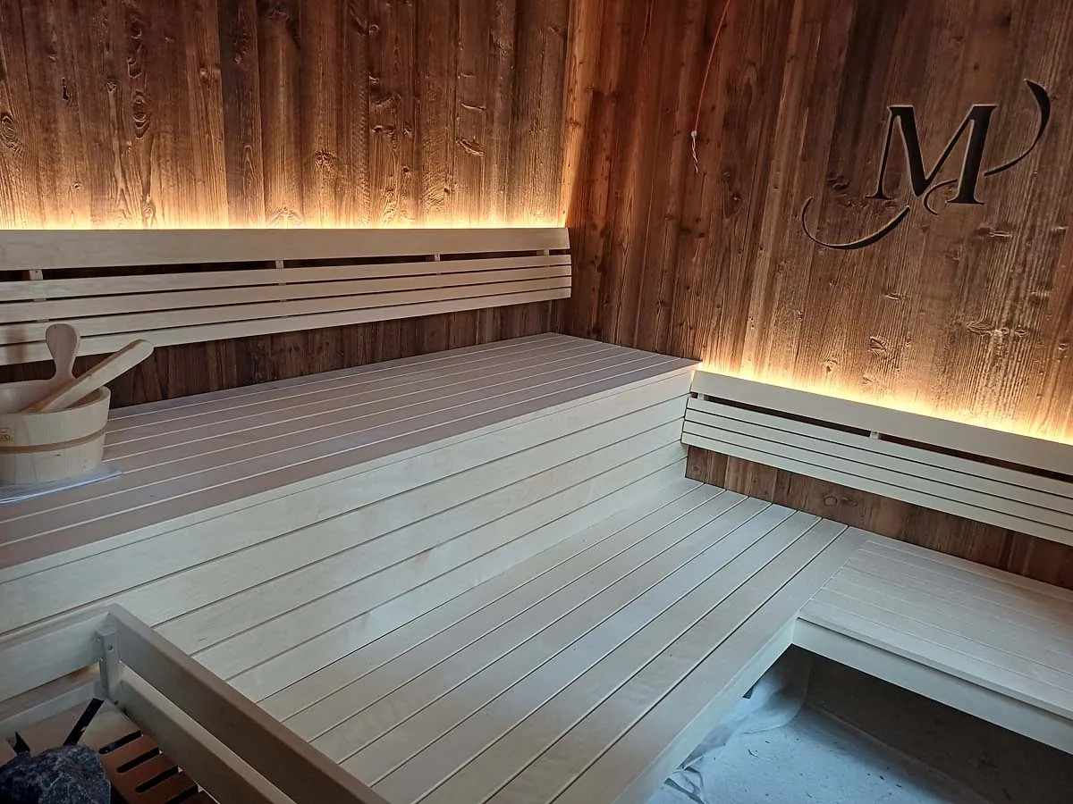 Sauna in dunklem Holz mit hellen Bänken und indirekter Beleuchtung