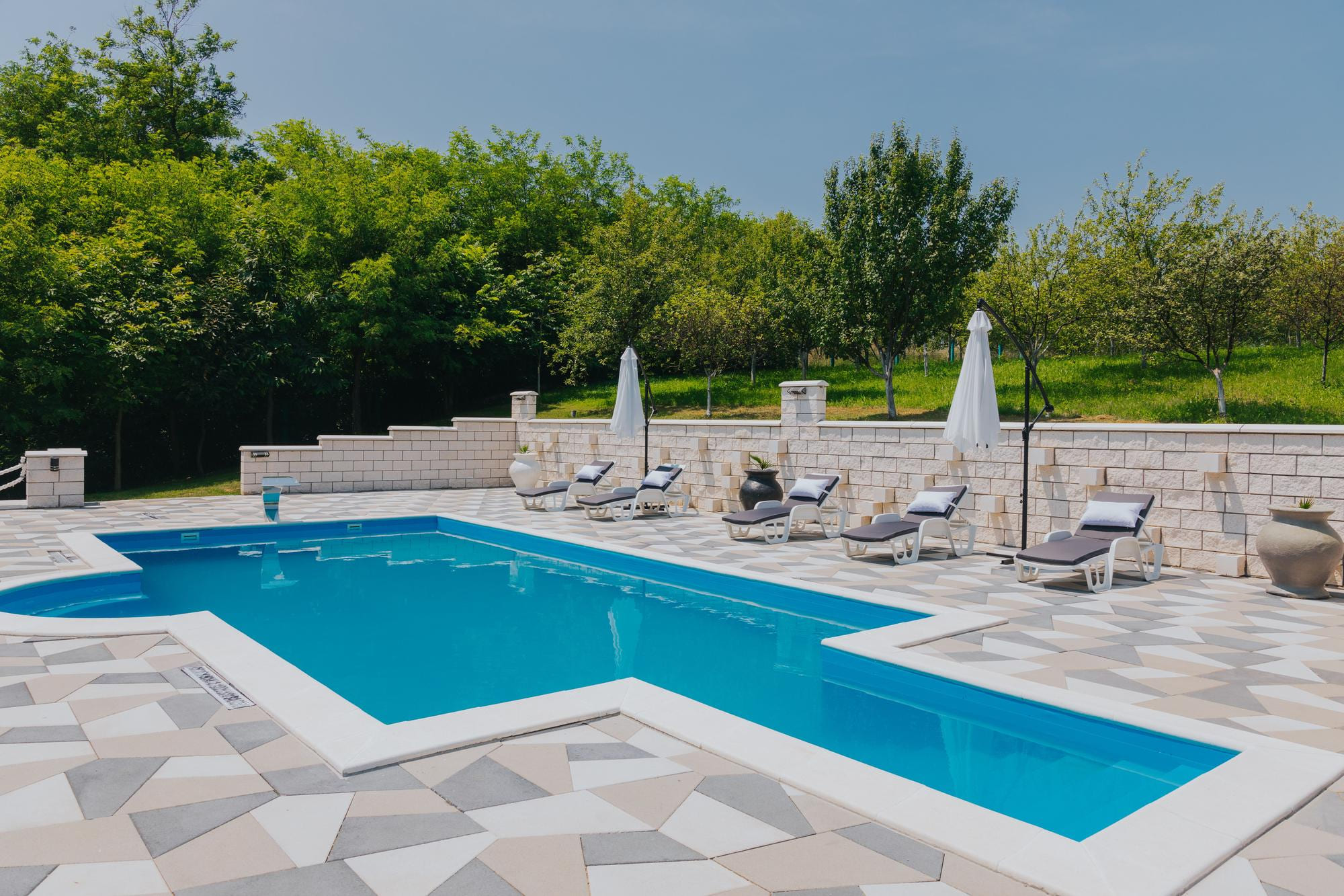 Pool mit gepflasterter Terrasse und Sonnenliegen vor Natursteinmauer