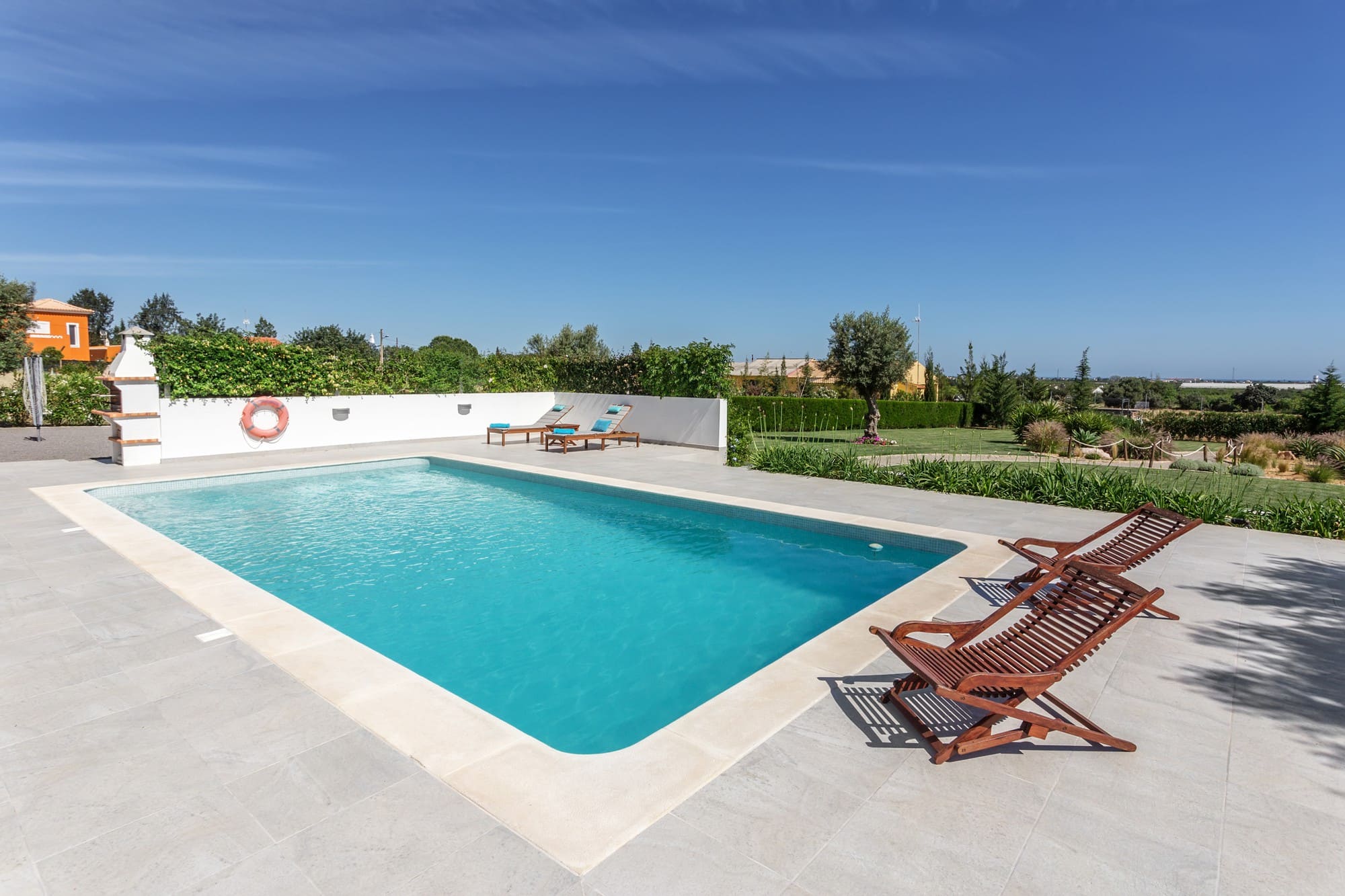 Eleganter Pool mit heller Steinterrasse, Olivenbaum und Holzliegen