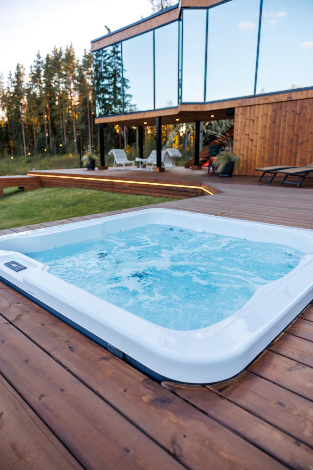 Whirlpool auf Holzterrasse vor modernem Glas-Wohnhaus im Wald