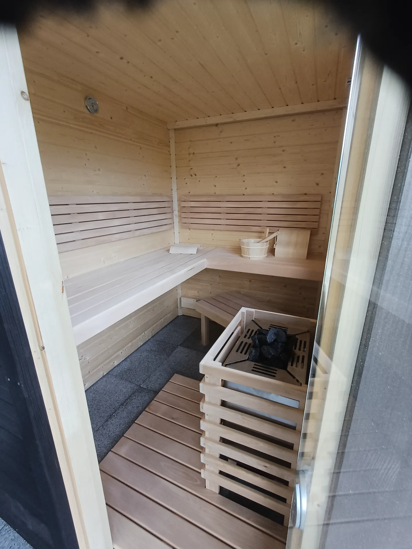 Saunainnenraum aus hellem Holz mit Eckbank, Saunaofen und Holzrost
